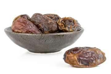 Group of six whole dry brown date fruit in dark ceramic bowl isolated on white background