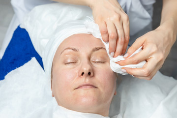 Fototapeta na wymiar Close-up beautician doctor hands making anti-age procedures, cleaning with napkins facial mask for mid-aged female client at beauty clinic. Cosmetologist doing skincare treatment .Health care therapy