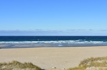 Fototapeta na wymiar Summer landscape with wild beach with waves breaking and blue sky. Arteixo, Coruña, Galicia, Spain.