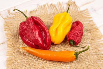 Group of four whole hot chili pepper on natural sackcloth on white wood