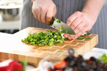 Chef Hands Holding Knife Cutting Green Onion. Man Chopping Scallion with Sharp Knife on Wooden Board at Kitchen. Fresh Greens for Dieting Cooking. Healthy Home Culinary Horizontal Photography