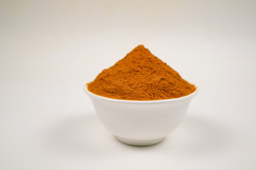 Turmeric powder in a separate white cup on a white background is used as a tonic for body and food ingredients.