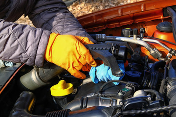 Fototapeta premium Car maintenance and repair concept. Hands of driver in orange rubber gloves checks car, open hood. Auto and vehicle repairing, close up.
