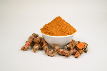 Turmeric powder in a white cup and isolated turmeric root on a white background is used as a tonic for body and food ingredients.