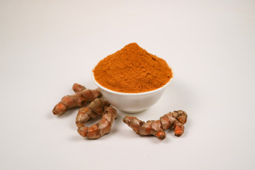 Turmeric powder in a white cup and isolated turmeric root on a white background is used as a tonic for body and food ingredients.