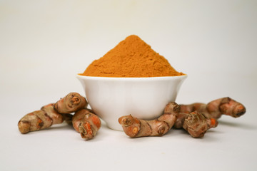 Turmeric powder in a white cup and isolated turmeric root on a white background is used as a tonic for body and food ingredients.