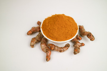 Turmeric powder in a white cup and isolated turmeric root on a white background is used as a tonic for body and food ingredients.