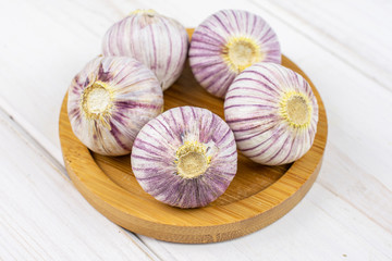Group of five whole fresh purple single clove garlic on bamboo coaster on white wood