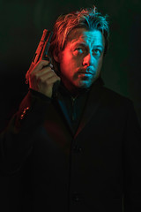 Man holding pistol next to his head. Illminated by red and blue light during the night.
