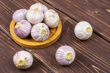 Lot of whole fresh purple single clove garlic on bamboo coaster on brown wood