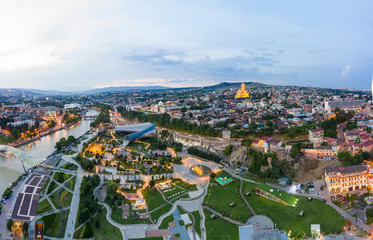 Panorama of the old town in the old district of Avlabari, Holy Trinity Cathedral and Rike Park, the Kura river reflects the evening city lights and cars traffic with blure in Tbilisi, Georgia