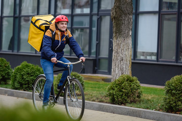 Obraz premium Selective focus of smiling delivery man with thermo backpack riding bicycle on urban street