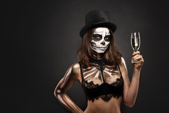 Halloween girl with skull makeup for Halloween on a black background holds champagne in her hands