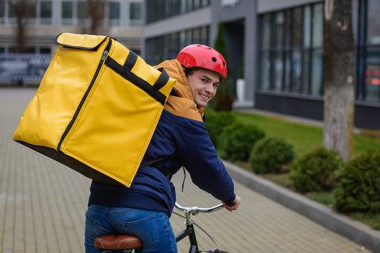 Back View Of Delivery Man With Thermo Backpack Smiling At Camera While Riding Bicycle On Urban Street