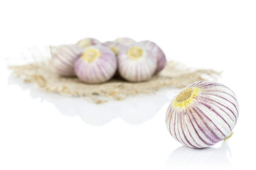 Lot of whole fresh purple single clove garlic on natural sackcloth isolated on white background