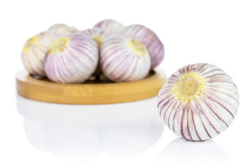 Lot of whole fresh purple single clove garlic on bamboo coaster isolated on white background