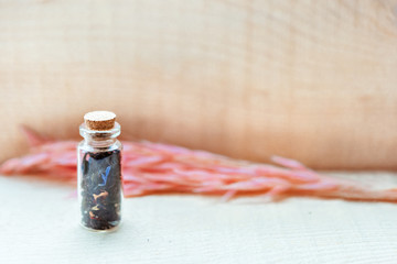 Small old vintage glass bottle with cork with floral tea and blue and pink petals on wooden background with spikelets . Organic healthy food and tea. Copy space for text