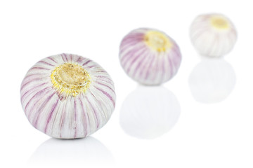 Group of three whole fresh purple single clove garlic placed diagonally isolated on white background