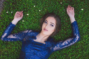 Beautiful girl in glamorous ultramarine dress lying on the grass.