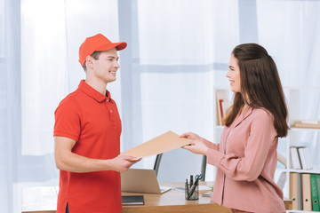 Obraz premium Side view of delivery man giving envelope to smiling businesswoman in office