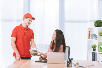 Delivery man giving takeaway salad to smiling businesswoman in office