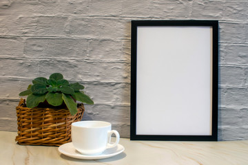 Front view of a blank mockup of black photo frame on brick wall background. A cup of coffee, flowers.