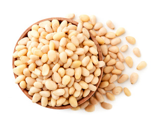 Pine nuts in a wooden plate and scattered on a white. The view of the top.