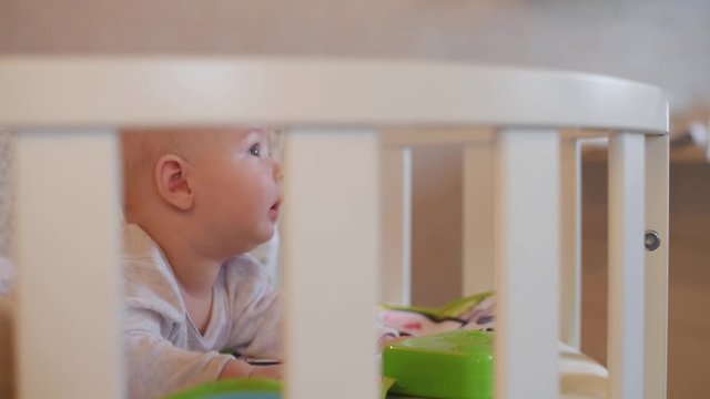 beautiful baby lies on his stomach in a crib and plays with a toy