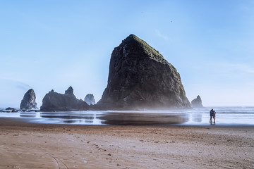 Haystack Rock at Cannon Beach, landmark of the Oregon Coast. Silhouette of a couple enjoying the view.