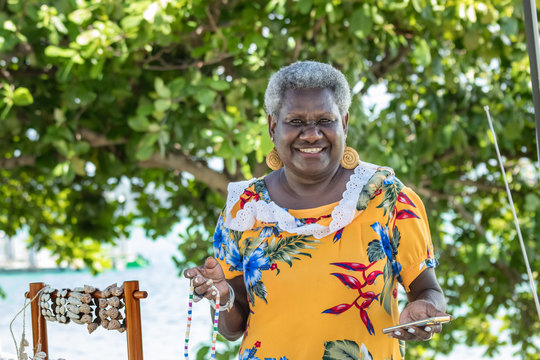 Portrait of a melanesian - australian mature woman smiling, possing at her stall holding a necklace that she has made, outdoors.