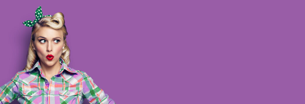 Portrait of excited surprised woman. Girl in pin up style, looking sideways. Retro fashion and vintage concept. Violet purpure color background. Copy space for some text.