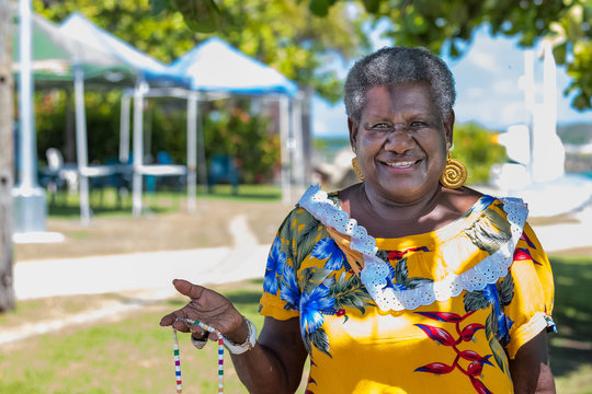 Portrait of a melanesian - australian mature woman smiling, showing the hand-made jewerly that she has made, outdoors.