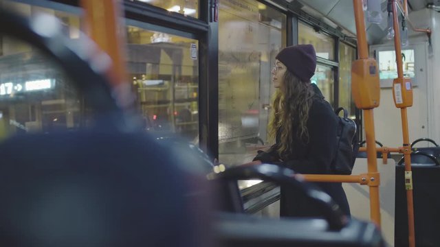 Medium shot of young curly-haired woman standing inside of bus and looking out of window