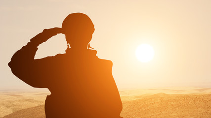 Silhouette Of A Solider Saluting Against the Sunrise in the desert of the Middle East. Concept -...
