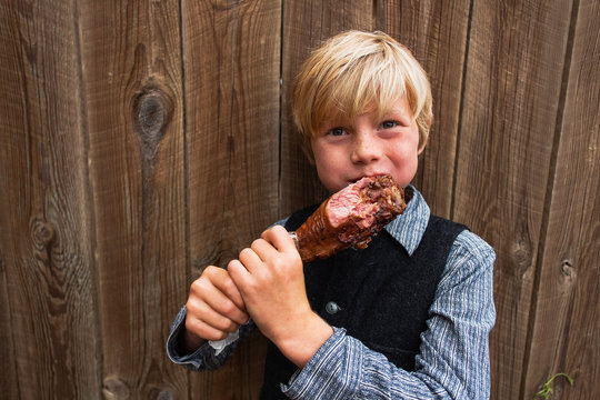 Boy standing by a fence eating a barbecued turkey leg, USA