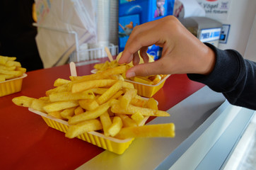 Oosterscheldekering, the Netherlands, August 2019. The main course at a street food kiosk: French fries. A portion is ready to be enjoyed, a hand is taking one.