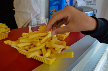 Oosterscheldekering, the Netherlands, August 2019. The main course at a street food kiosk: French fries. A portion is ready to be enjoyed, a hand is taking one.