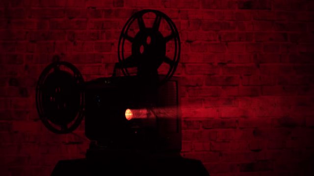 Silhouette of a 16mm film projector with a seedy red light background.