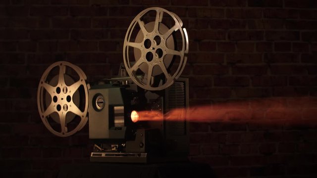 Wide shot of a home movies projector playing in the dark with volumetric light beaming from the bulb.