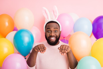 Photo of funny dark skin guy colorful decorations easter party hold arms like rabbit paws obedient person wear sweater bunny ears on balloons pink color background
