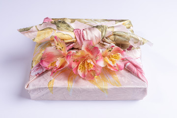 Close-up trendy wrapped in floral textile in Furoshiki technique gift box with flowers Alstroemeria on grey background.