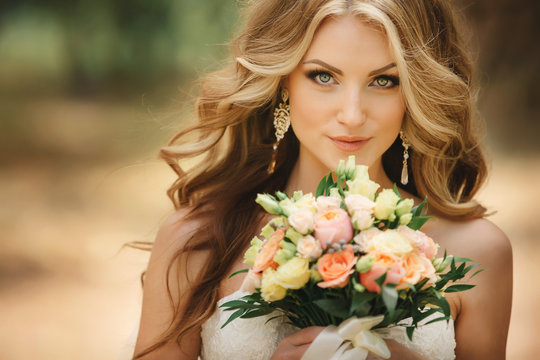 Portrait of beautiful luxury bride with roses wedding bouquet outdoors. Young woman with professional make up and hair style. Wedding day. Marriage.
