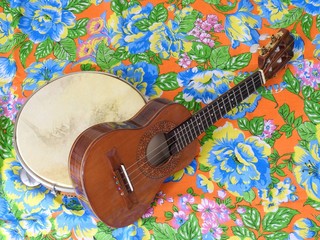 Two Brazilian musical instruments: cavaquinho and pandeiro (tambourine) on a very colorful “chitao” fabric with large floral prints. They are widely used to accompany samba and choro music.