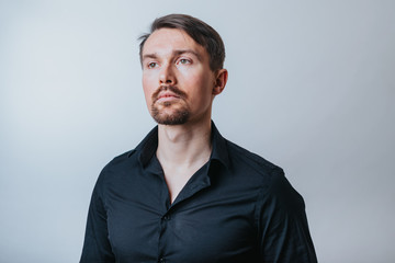 Photo of a handsome man with a coolly stylized scrub and hairstyle. Photo taken in a photo studio on a gray background. The man tries to express his emotions with gesticulation and mimics.