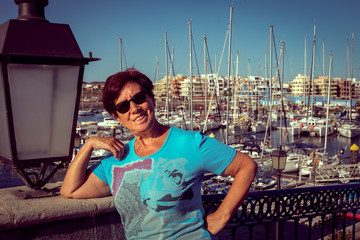 Wonderful view of the harbour. Close up of an attractive senior woman. One person in vacation or retirement. Harbor and boats in background. Blue sky. Relaxation under the tropical sun