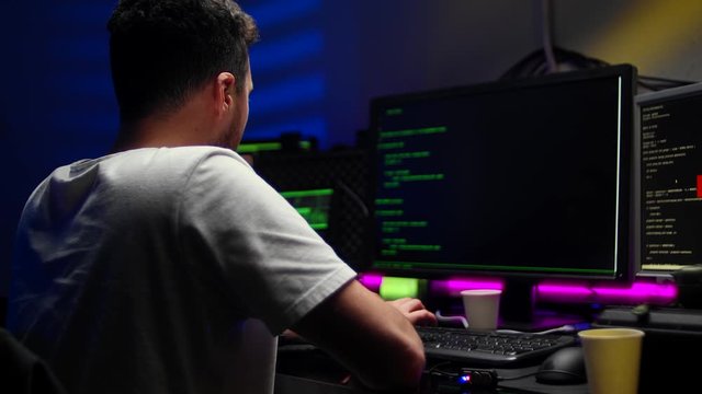 cybercrime, hacking and technology concept - male hacker writing code or using computer virus program for cyber attack and drinking coffee in dark room at night
