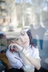 Girl behind the glass in a cafe. Portrait of a blower through the window of a coffee shop.