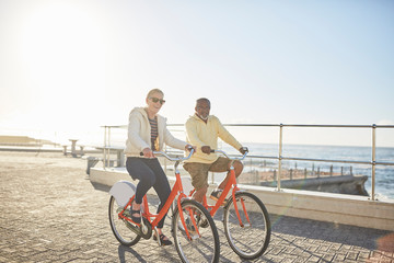 Happy senior couple bike riding on sunny ocean boardwalk