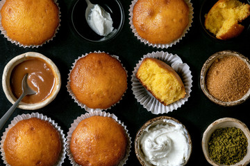 Homemade citrus oranges or clementines sweet muffins cakes in baked tray with different toppings above over wooden cutting board as background. Flat lay, close up