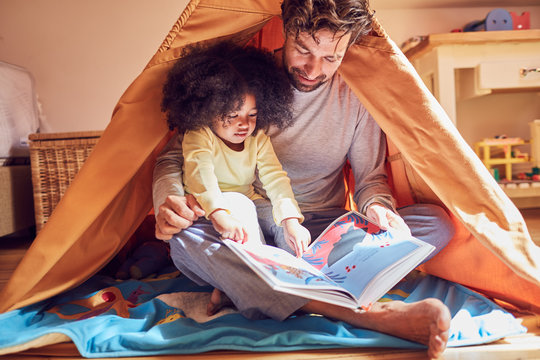Father and daughter reading book in teepee